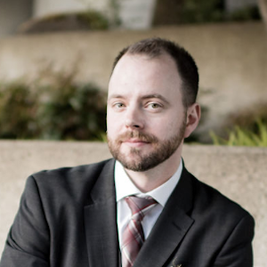 Man with beard in black suit looks toward the camera