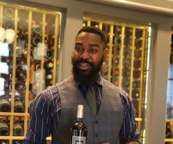 Man holding wine bottle stands in front of wine rack