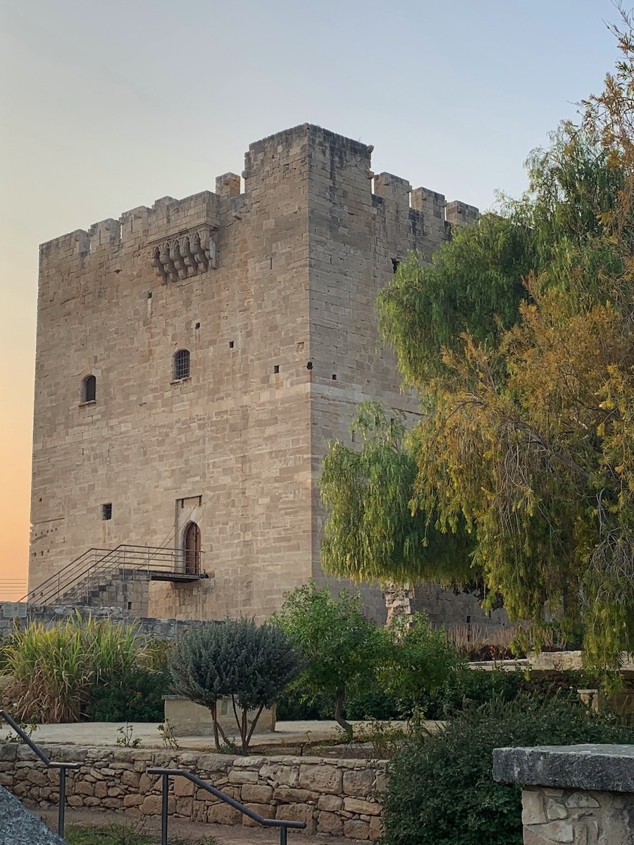 Tall, sharp-edged castle made of gray bricks with leafy trees nearby